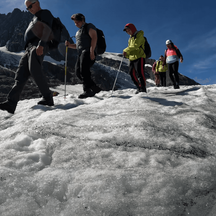 A group of youth hikers follow a mountain guide across a glacier.